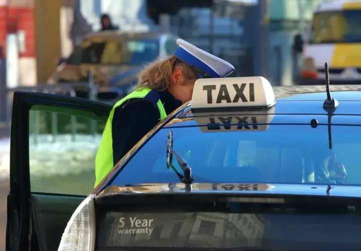 Kontroler drogowy w kamizelce odblaskowej pochyla się nad taksówką, sprawdzając dokumenty. Może to oznaczać mandat za brak pasów.