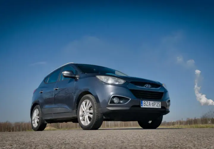 Szary Hyundai ix35 na tle błękitnego nieba. W tle komin z dymem. Wiele pozytywnych hyundai ix35 opinie potwierdza jego wszechstronność.