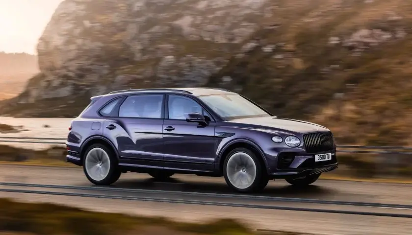 Fioletowy Bentley SUV pędzi po górskiej drodze, otoczony jesiennym krajobrazem.