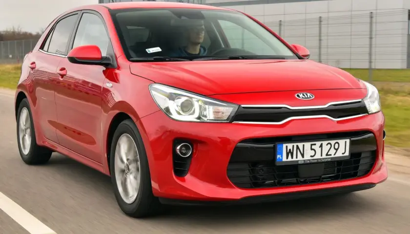 Czerwony Kia Rio 4 w ruchu, z kierowcą za kierownicą.