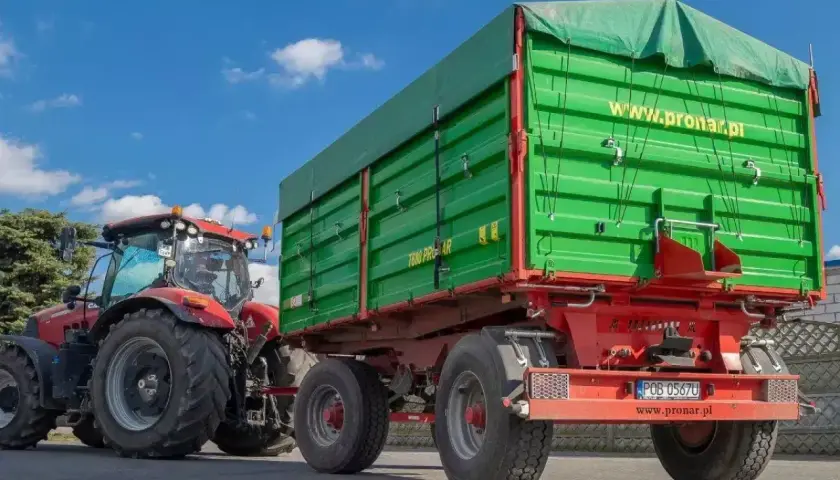 Czerwony traktor z zieloną przyczepą. Zastanawiasz się, ile można jechać z przyczepką? Ten zestaw jest gotowy do pracy.