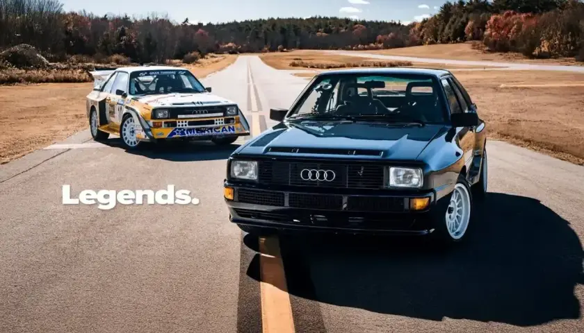 Dwa kultowe Audi S1 Quattro, jeden czarny, drugi w barwach rajdowych, stoją na pustej drodze.