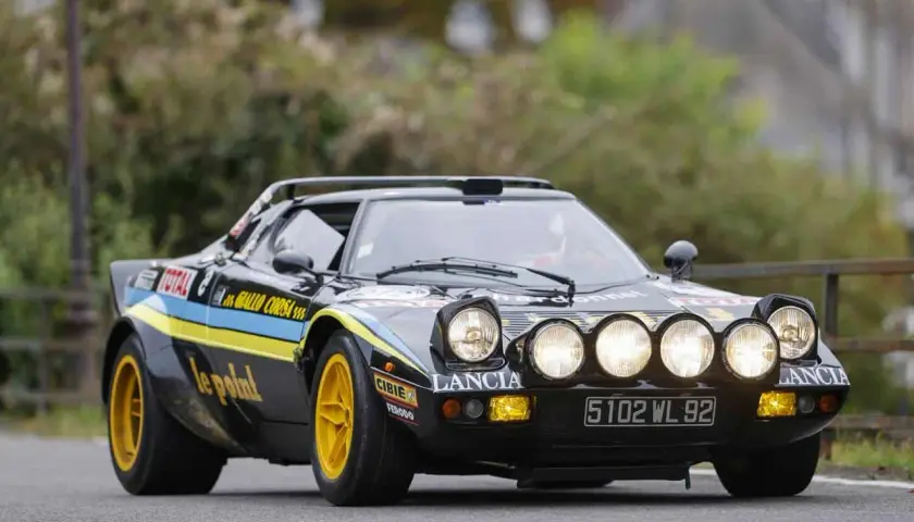Czarny Lancia Stratos z żółtymi felgami i rajdowymi oznaczeniami, gotowy do pokonania kolejnego zakrętu.