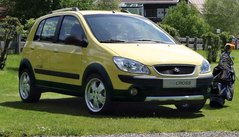 Żółty Hyundai Getz Cross zaparkowany na trawie obok torby golfowej.