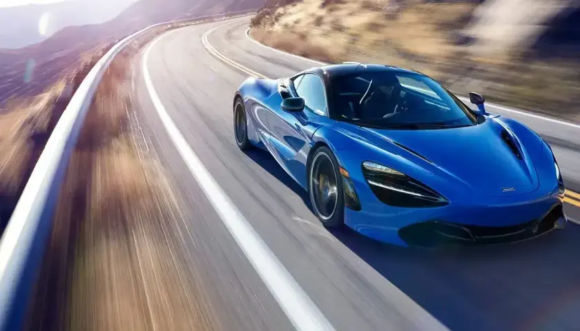 Niebieski McLaren 720S pędzi po krętej górskiej drodze, tworząc rozmyte smugi światła i cienia.
