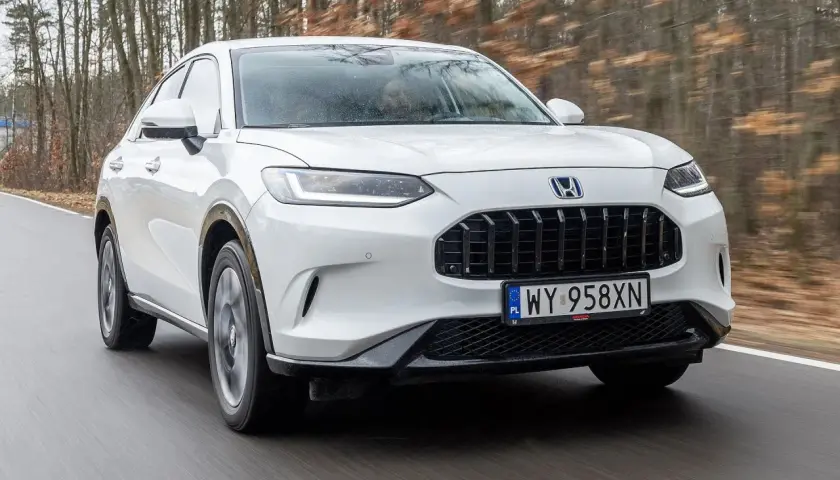 Biała Honda ZR-V przemierza leśną drogę, ukazując swój elegancki design i dynamiczną sylwetkę.