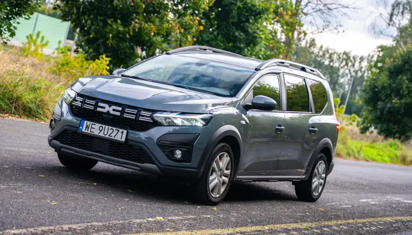 Szare auto 7 osobowe Dacia Jogger na tle zieleni. Idealne na rodzinne wycieczki.