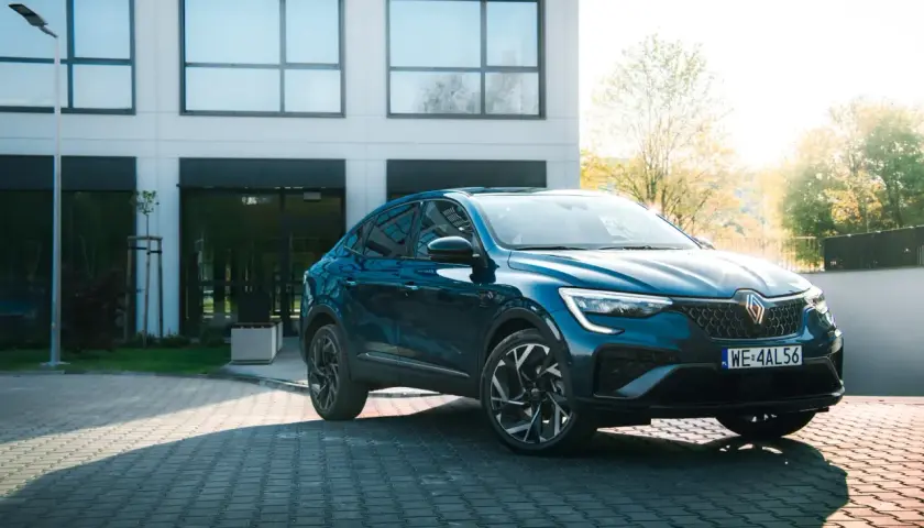 Elegancki, granatowy Renault Arkana na tle nowoczesnego budynku. Sprawdź, jaka jest jego renault arkana cena i możliwości.