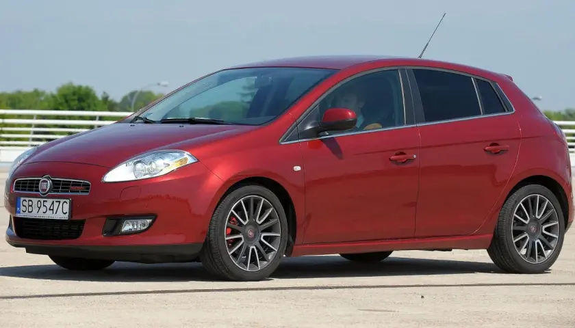 Czerwony Fiat Bravo z kierowcą za kierownicą, zaparkowany na zewnątrz.