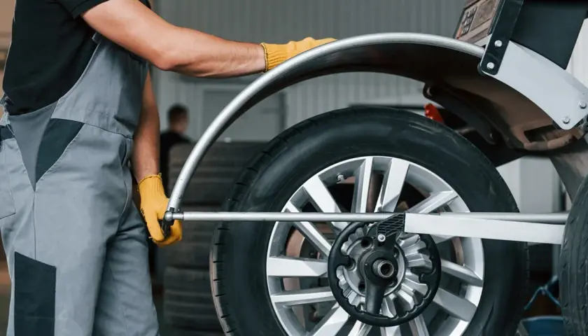 Mechanik w żółtych rękawiczkach ustawia koło na wyważarce. Dowiedz się, ile kosztuje wyważenie kół.
