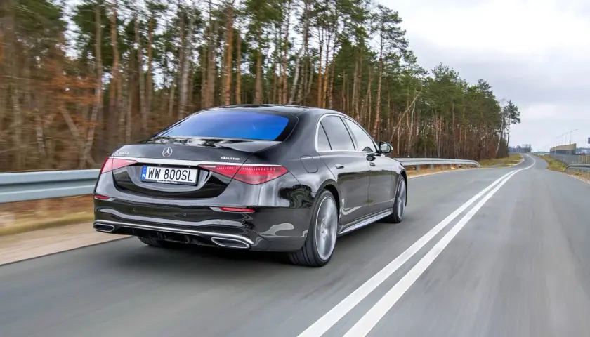 Czarny Mercedes S400d 4Matic sunie po drodze wśród drzew.