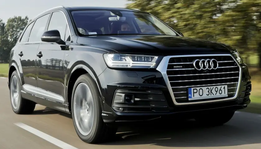 Czarny Audi Q7 3.0 TDI pędzi po drodze, otoczony zielenią drzew.