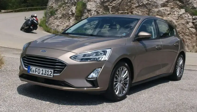 Brązowy Ford Focus MK3 1.6 TDCI na krętej drodze, z motocyklistą w tle.