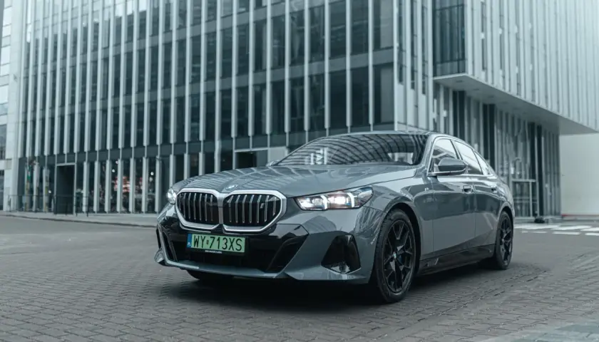 Eleganckie, szare BMW i5 z czarnymi felgami stoi przed nowoczesnym budynkiem biurowym.
