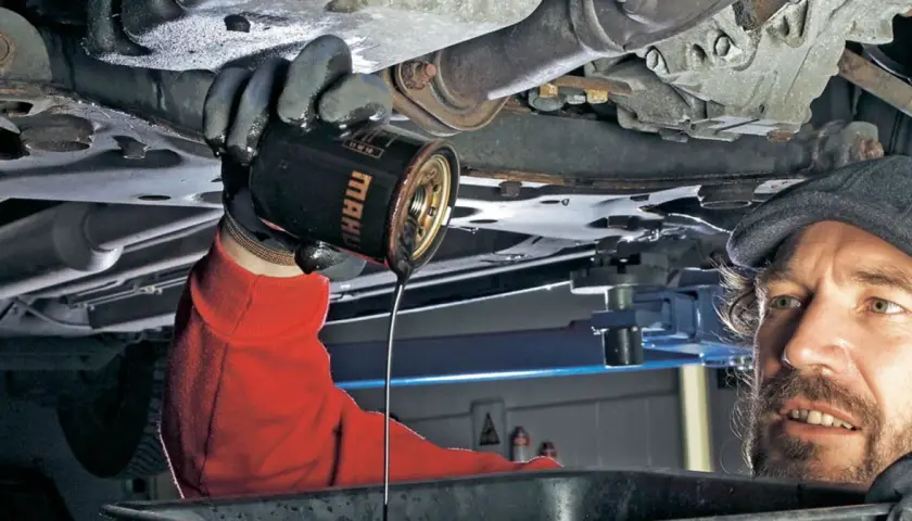 Mechanik w czerwonej bluzie wymienia stary olej z silnika. Pamiętaj, co ile wymiana oleju, by auto służyło latami.