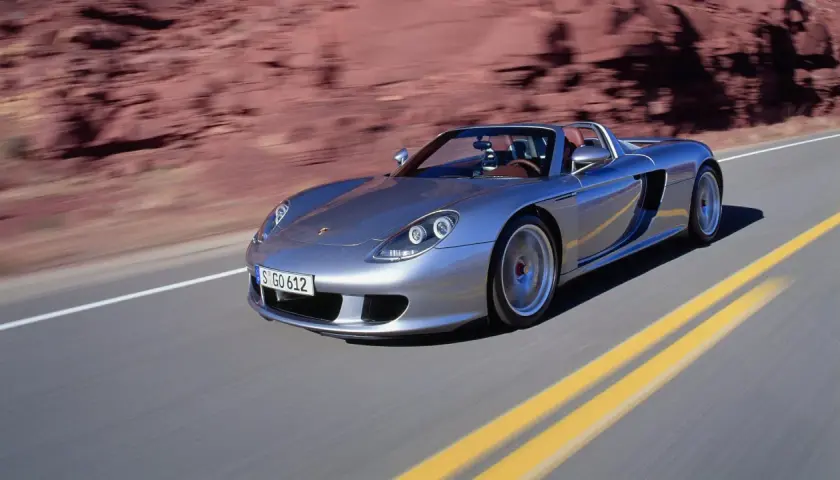 Srebrny Porsche Carrera GT pędzi po pustynnej drodze, zostawiając za sobą rozmyte czerwone skały.