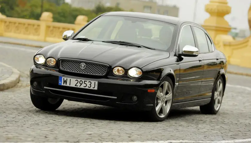 Czarny Jaguar X Type na brukowanej ulicy, z charakterystyczną atrapą chłodnicy i okrągłymi reflektorami.