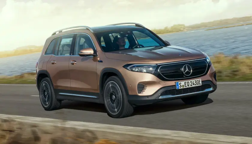 Brązowy Mercedes EQB jedzie po drodze nad jeziorem.