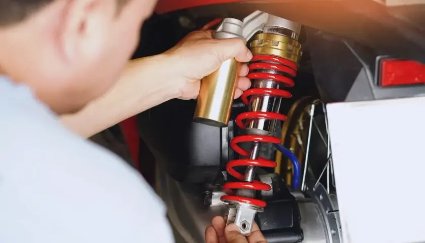 Mechanik dokonuje wymiany amortyzatorów w motocyklu, trzymając nowy element.