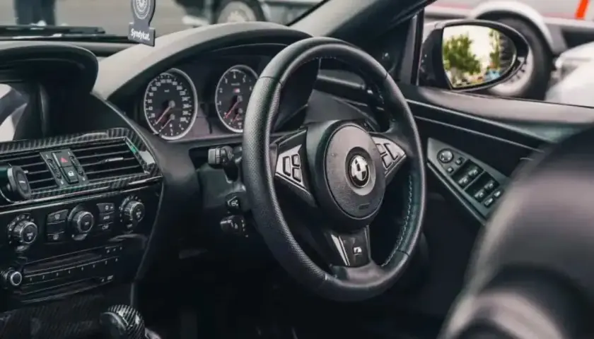 Wnętrze BMW E64 z czarną kierownicą, deską rozdzielczą i karbonowymi wstawkami.