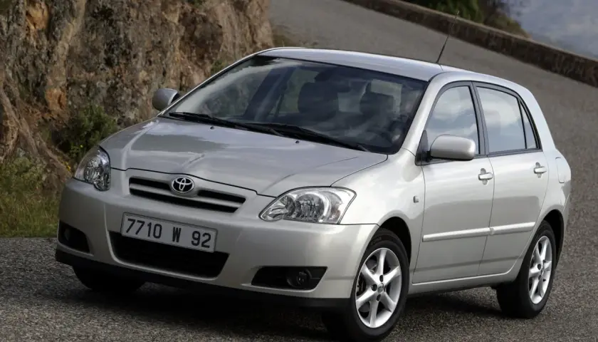 Srebrna Toyota Corolla E12 hatchback na krętej drodze wśród skał i zieleni.