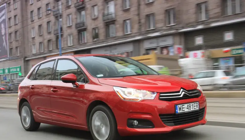 Czerwony Citroen C4 1.6 HDi w ruchu miejskim, z rozmytym tłem budynków i innych pojazdów.