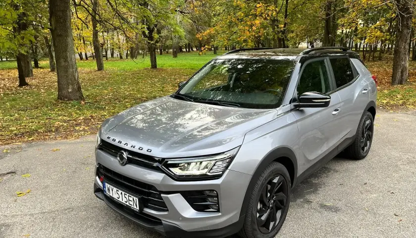 Srebrny SsangYong Korando na tle jesiennego parku. Wiele pozytywnych ssangyong korando - opinie użytkowników potwierdza jego wszechstronność.