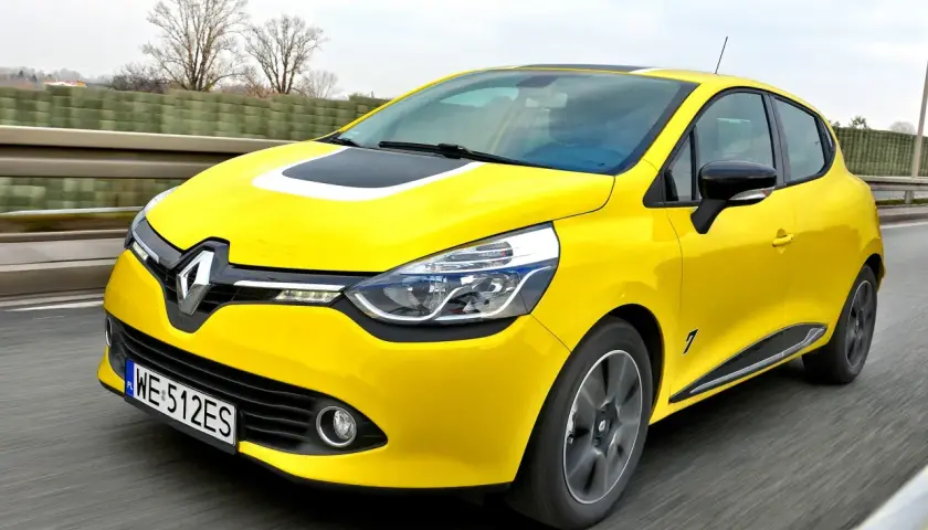 Żółty Renault Clio, jeden z popularnych francuskich marek samochodów, pędzi po drodze.