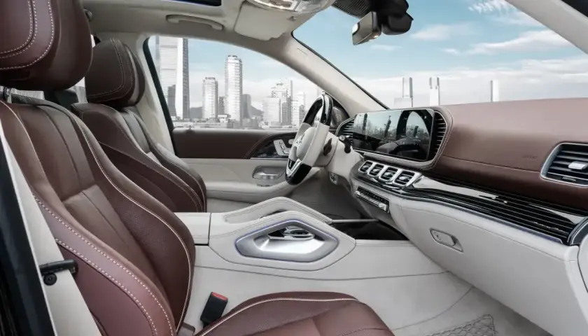 Wnętrze luksusowego **Mercedes GLS 2025** z brązową skórzaną tapicerką i nowoczesnym panelem. Widok na miasto przez panoramiczny dach.