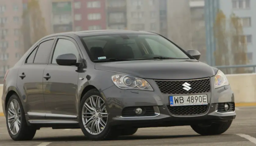 Szary Suzuki Kizashi z polskimi tablicami WB 4890E zaparkowany na tle bloków mieszkalnych.