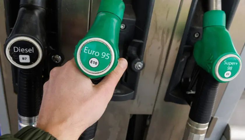 Dłoń wybiera dystrybutor z napisem "Euro 95 E10", czyli benzyna bezołowiowa. Obok widać dystrybutory Diesel i Super+ 98.