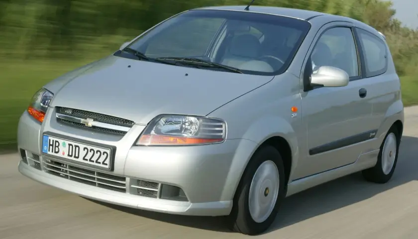 Srebrny Chevrolet Kalos w wersji 3-drzwiowej jedzie po drodze, rozmyte tło sugeruje ruch.