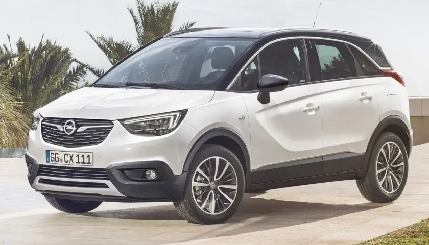 Biały Opel Crossland z czarnym dachem, zaparkowany na tarasie przy basenie. Wiele osób szuka opinii o tym modelu.