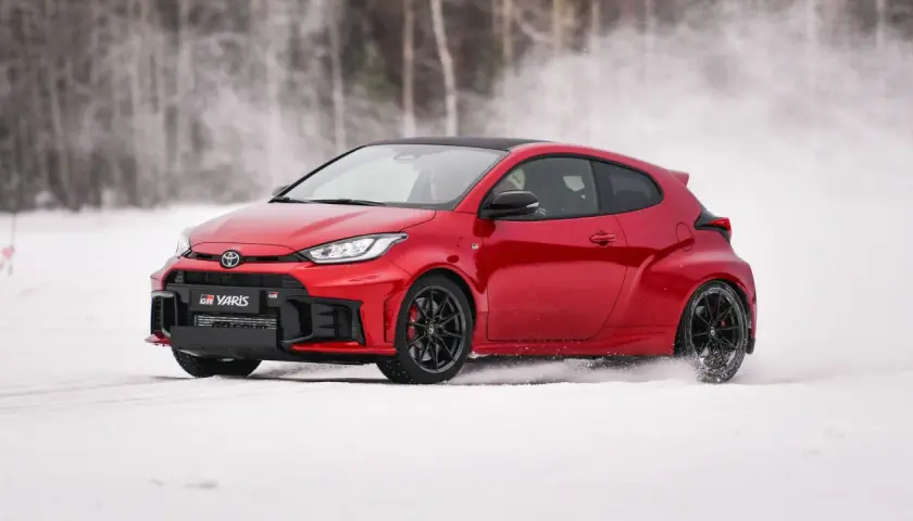Czerwony Toyota GR Yaris driftuje po śniegu, tworząc obłoki białego puchu.