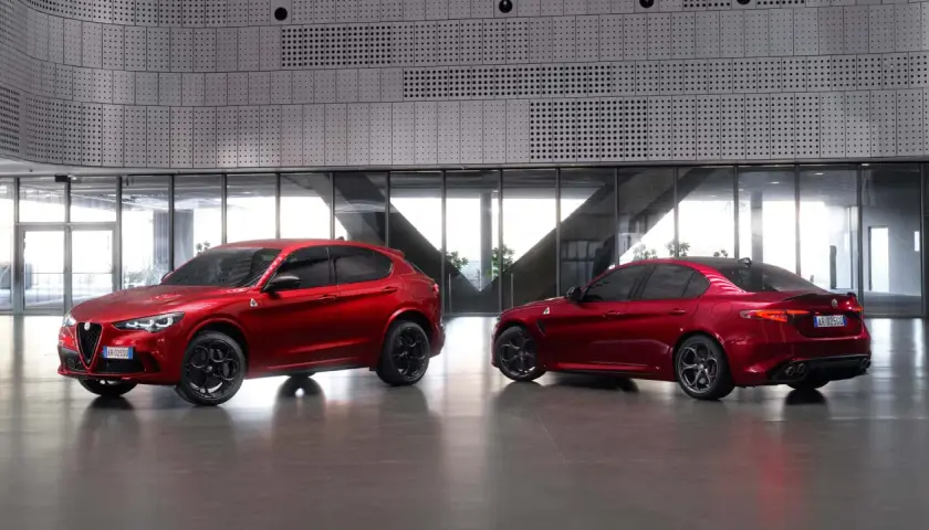 Dwa czerwone Alfa Romeo, SUV Stelvio i sedan Giulia Quadrifoglio, stoją obok siebie w nowoczesnym wnętrzu.