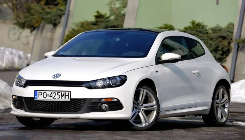 Biały Volkswagen Scirocco z czarnym dachem, zaparkowany na zewnątrz.