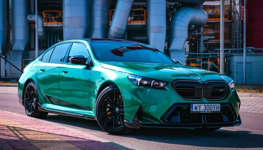 Błyszczące, zielone BMW M5 G90 na tle przemysłowej infrastruktury.