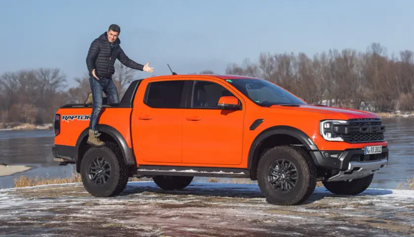 Pomarańczowy Ford Ranger Raptor z kierowcą na pace, gotowy na zimową przygodę nad rzeką.