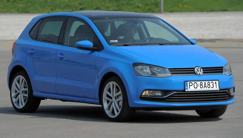 Niebieskie polo 6r z czarnym dachem, zaparkowane na zewnątrz. Kierowca siedzi za kierownicą.