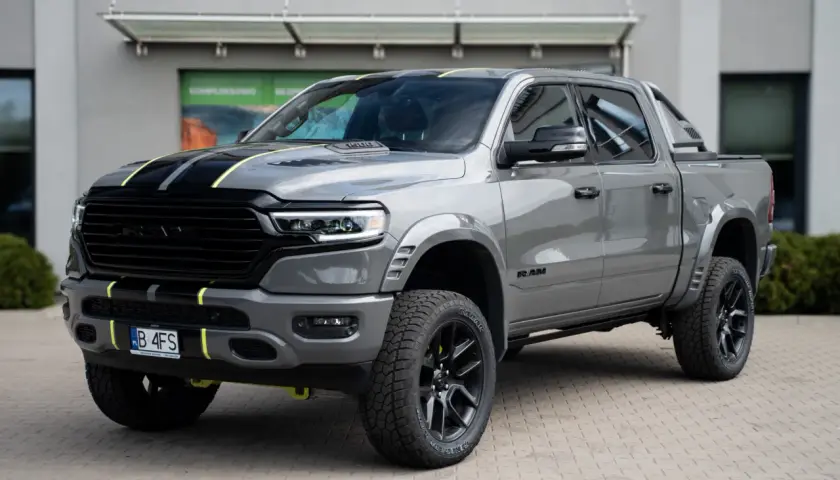 Szary Dodge Ram 1500 z żółtymi akcentami i czarnymi pasami na masce, zaparkowany przed budynkiem.