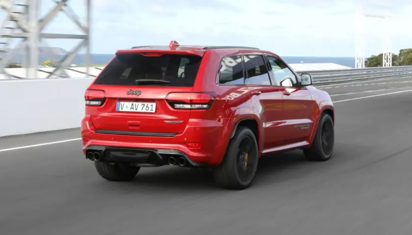 Czerwony Jeep Grand Cherokee Trackhawk SRT pędzi po torze wyścigowym, jego potężny silnik brzmi jak burza.