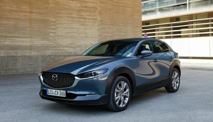 Szary Mazda CX-30 stoi przed betonową ścianą. Wady tego modelu to m.in. ograniczona widoczność z tyłu.