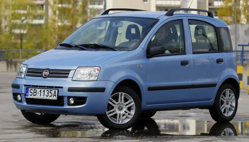 Niebieski Fiat Panda z kierowcą, stojący na mokrej nawierzchni. Kierowca zastanawia się nad aktualną ceną gazu.