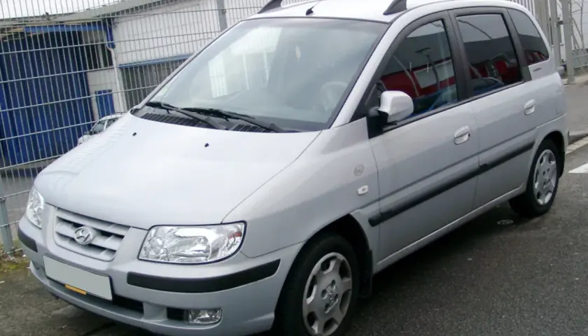 Srebrny Hyundai Matrix stoi przed budynkiem z niebieskimi drzwiami i metalowym ogrodzeniem.