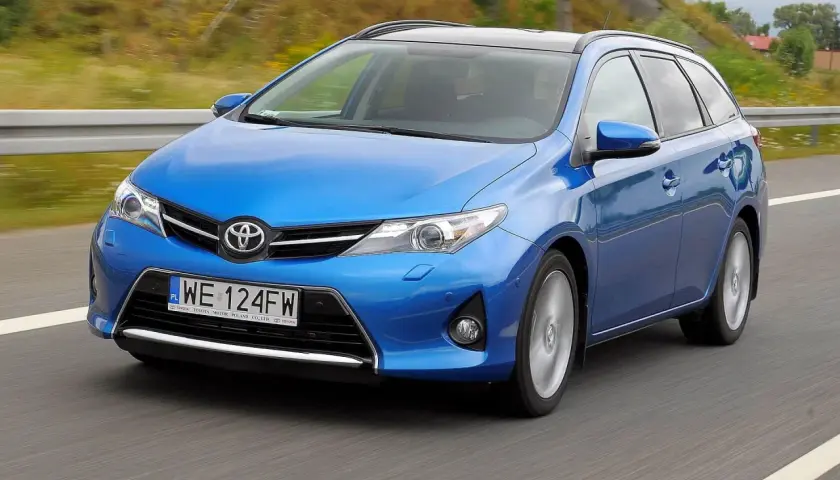 Niebieski Toyota Auris 1.6 benzyna w wersji kombi jedzie po drodze.