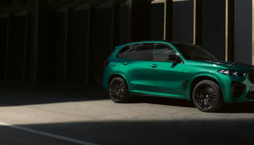 Zielony BMW X5 M z czarnymi felgami stoi na tle ciemnej architektury, oświetlony pasem światła.