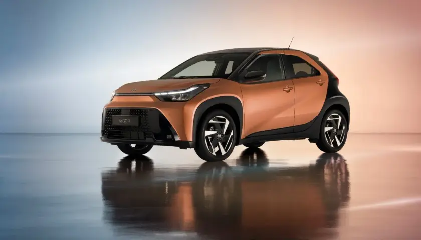 Pomarańczowy Toyota Aygo Cross z czarnymi akcentami i stylowymi felgami, odbijający się w lustrzanej podłodze.