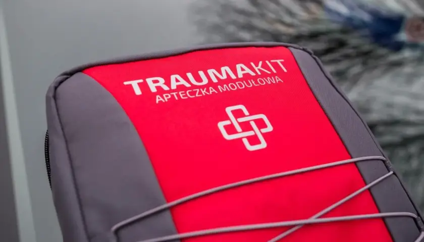 Czerwono-szara apteczka "Trauma Kit" z symbolem krzyża. Czy apteczka jest obowiązkowa w samochodzie? Zawsze warto ją mieć!