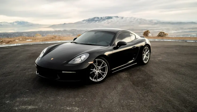 Czarne Porsche Cayman na tle gór i jeziora. Zastanawiasz się, ile kosztuje Porsche?