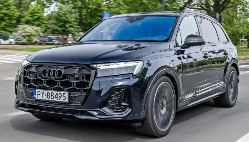Ciemny Audi Q7 w ruchu ulicznym. Zbliżenie na przednią część pojazdu, widoczna atrapa chłodnicy i reflektory. Poznaj audi q7 wymiary.